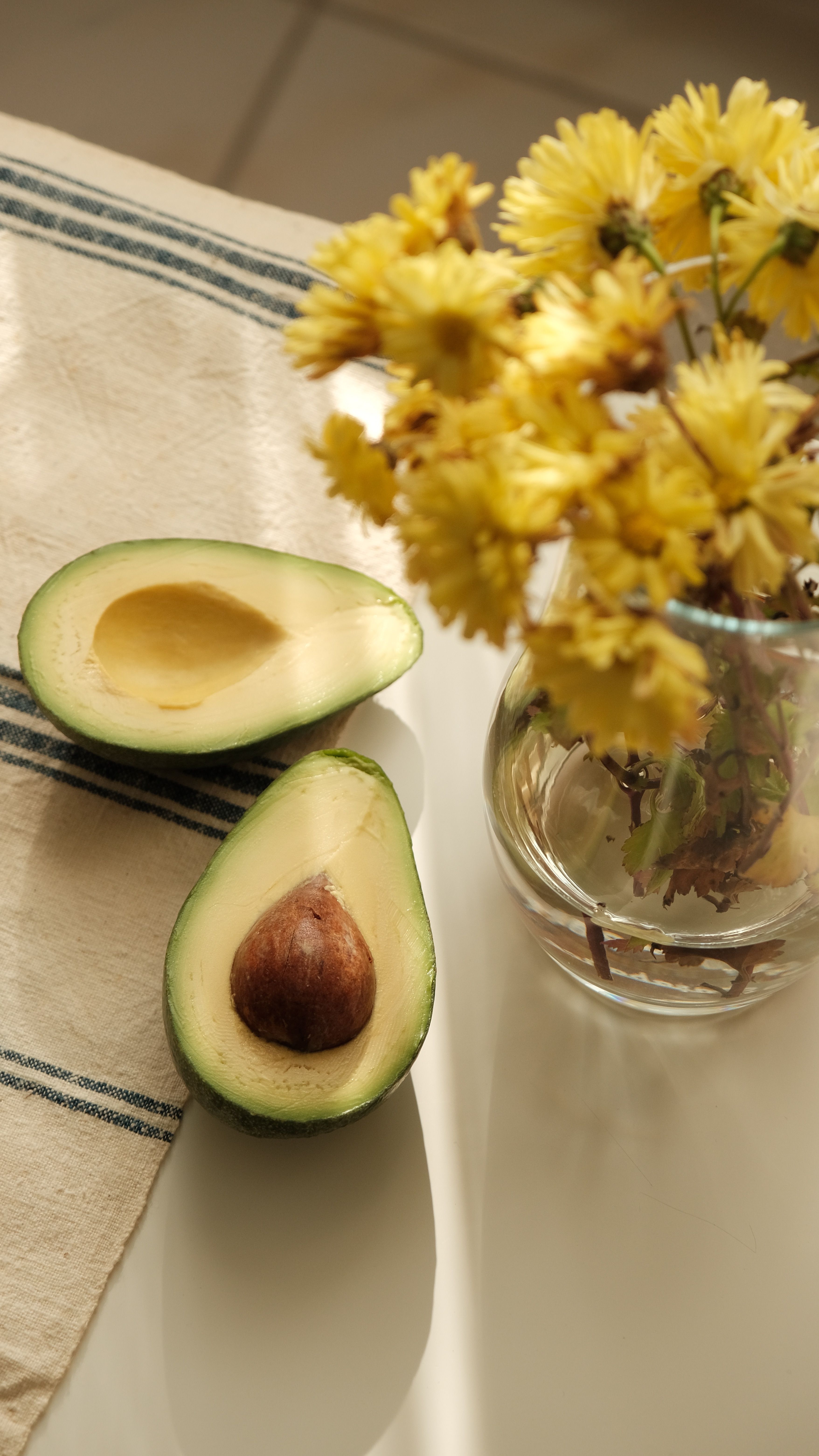 Aguacate cortado por la mitad junto a flores amarillas — comida real y bonita